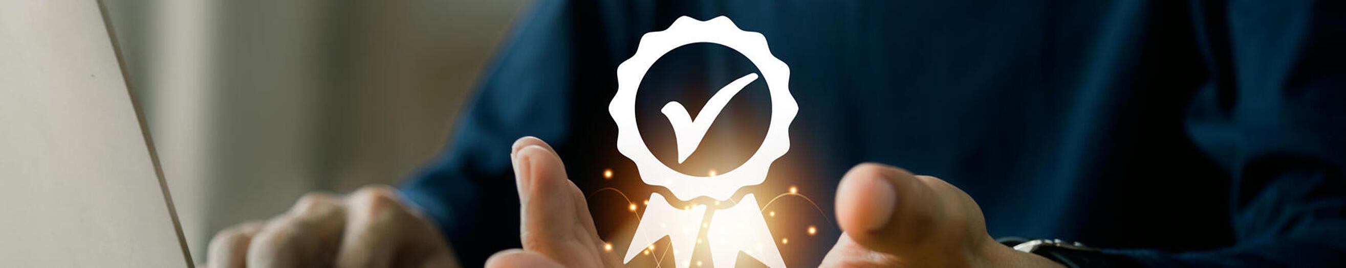 Mensch sitzt vor einem Laptop und hält die Hand hoch